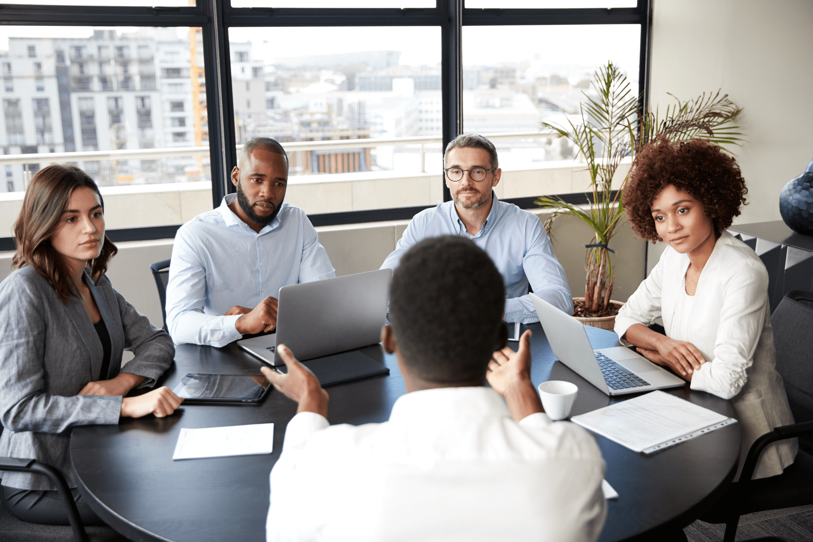 A board meeting around a table with laptops and papers
